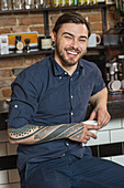 Portrait of cheerful hairdresser sitting with coffee at bar counter in barber shop