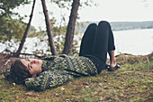 Side view portrait of woman lying on field by lake