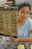 Indonesia, Bali, Tenganan, animist village. Portrait of a saleswoman of Ramayana (short history of epic mythological ) on palm leaves dried.