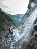 Junge Wanderin betrachet einen Wasserfall in der Nähe der Kemptener Hütte in den Alpen