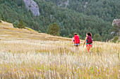 Two Female Hiker Walking On Trail Covered By Tall Grassy Landscape