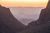 A Vast Desert Mountain Landscape Seen Through A V-shaped Rock Formation As The Sun Sets In The Distance