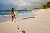 A Surfer Girl Walking On The Beach Towards A Rainbow On The North Shore Of Oahu