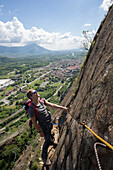 Young man ascends via ferrata, valley below