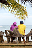 Rear View Of A Couple Sitting On Bench Exploring Ocean