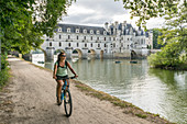 Girl cycling with Chenonceau castle on the background, UNESCO World Heritage Site, Chenonceaux, Indre-et-Loire, Centre, France, Europe