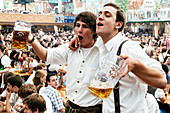 Young men in leather trousers standing on beer benches celebrate Oktoberfest in the beer tent