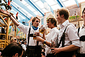 Junge Männer in Lederhosen auf den Bierbänken feiern Oktoberfest im Bierzelt