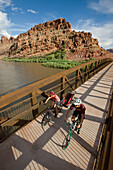 Ashley Korenblat, Mark Sevenoff biking on the pedestrian bridge going over the Colorado river in Moab, Utah.