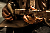 Detail of a man playing a Central Asian instrument similar to a guitar.