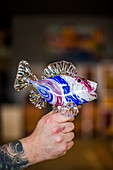 A man holds a glass sculpture of a fish in his hand at a glass blowing studio on Whidbey Island, WA.
