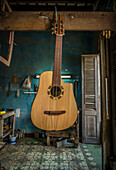 'A recently finished Cuban tres'' hangs in a hand-made guitar workshop in Havana, La Habana, Cuba. The workshop is seen in the background.'''