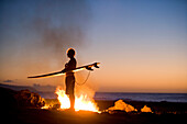 A surfer stands by a campfire at  Rocky Point, on the North Shore of Oahu, Hawaii, 09.04.08.