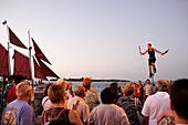A juggler atop a tall unicycle performs in front of a large crowd of tourists at the famous Key West boardwalk after sunset.