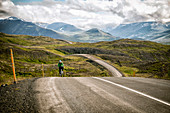 A Woman Cyclist Crests A Hill In The Mountains Of North Iceland