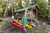Two Men Carry Kayaks Past The Cabins At The Lodge Near Greenville, Maine