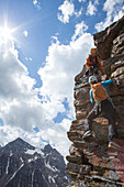 Mountain guide assists woman climber up rock face above mountains