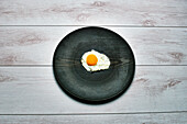 Draufsicht auf ein Ei und ein schwarzes Teller auf einem weißen Holztisch
