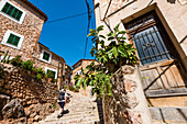 Eine Wanderin in einer Gasse im malerischen kleinen Bergdorf im Tramuntanagebirge, Fornalutx, Mallorca, Spanien