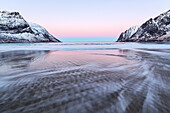 Das rosa Licht des Sonnenaufgangs über die Wellen des gefrorenen Meeres, umgeben von schneebedeckten Gipfeln, Ersfjord, Senja, Troms, Norwegen, Skandinavien, Europa