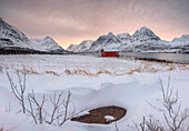 Panorama von rosa Himmel in der Morgendämmerung auf der Holzhütte umgeben von gefrorenem Meer und schneebedeckten Gipfeln, Svensby, Lyngen Alpen, Troms, Norwegen, Skandinavien, Europa