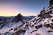 Wanderer auf Gipfel Hesten bewundert den Berg Segla und den Mefjord, der von einem gefrorenen Meer bei Sonnenaufgang, Senja, Troms, Norwegen, Skandinavien, Europa umrahmt ist