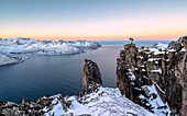 Fotograf auf den Felsen auf dem Berg Hesten bewundert den Mefjorden und das gefrorene Meer bei Sonnenaufgang, Senja, Troms, Norwegen, Skandinavien, Europa