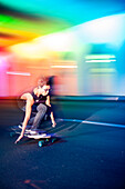 Junger Mann skateboarding in bunt beleuchtetem Verkehrstunnel