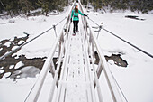Woman hiking across footbridge in winter