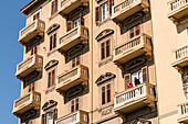 Italian house front with balconies on Piazza Verdi square with two men talking on one balcony, Palermo, Sicily, Italy, Europe
