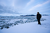 Man overlooks Jökulsárlón (Jokulsarlon) Glacier Lagoon in snowy winter landscape during the last light of the day, Jökulsárlón (Jokulsarlon), Iceland, Europe