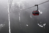 'Red gondola lift in the clouds with forest covered mountains below; Whistler, British Columbia, Canada'