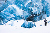 A man on a split board views a large wall of ice at the Canwell Glacier, Interior Alaska, USA
