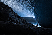 Ein Mann erleuchtet einen dunklen Tunnel unter dem Eis des Canwell Gletschers mit einer Taschenlampe, Innenraum Alaska, USA