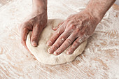 Hände arbeiten mit Pizzateig auf einer hölzernen bemehlten Oberfläche