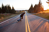 Ein junger Mann skateboarding eine Straße in der Dämmerung, Homer, Alaska, Vereinigte Staaten von Amerika