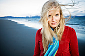 Portrait einer jungen Frau, die am Strand am Rand des Wassers steht, mit ihrem langen blonden Haar, das im Wind weht, Homer, Alaska, Vereinigte Staaten von Amerika