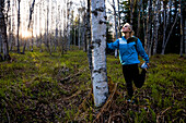 Eine junge Frau, die ihre Beine vor einem Lauf in einem Wald streckte, Homer, Alaska, Vereinigte Staaten von Amerika
