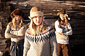 Portrait of three girls standing by a log cabin wearing fur hats, Homer, Alaska, United States of America