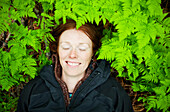 Eine Frau legt den Kopf auf den Waldboden unter den hellgrünen, üppigen Farnen, Alaska, Vereinigte Staaten von Amerika