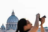 Eine Touristin schießt Fotos mit dem  Petersdom Basilica di San Pietro im Hintergrund, Rom, Latium, Italien