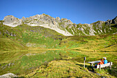 Two persons sitting on bench and looking towards lake Iglsee with Wildkarkopf, valley Riedingtal, Radstadt Tauern, Lower Tauern, Carinthia, Austria