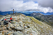 Two persons hiking sitting at summit of Jakobspitze, Jakobspitze, Sarntal Alps, South Tyrol, Italy