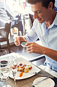Mann mit Smartphone, um sein Essen im Restaurant zu fotografieren