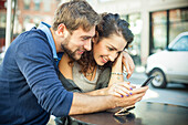 Couple sitting outdoors together, looking at smartphone