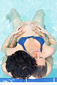 Pregnant woman with partner relaxing in swimming pool