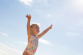 Kleines Mädchen steht am Strand mit erhobenen Armen