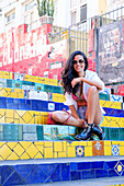 Junge brasilianische Frau mit Sonnenbrille sitzt auf der Selaron Schritte in Lapa, Rio de Janeiro, Brasilien, Südamerika