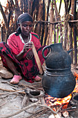 Eine Frau bläst durch eine Holzpfeife, um das Feuer beim Kaffeebrühen auf offenem Feuer, Äthiopien, Afrika