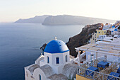 Evening view over the Caldera from Oia with blue domed church and distant volcanic cliffs, Santorini, Greek Islands, Greece, Europe